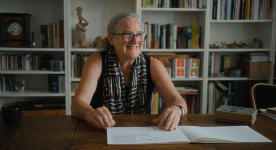 Barbara Buser sitzt am Schreibtisch und grinst.